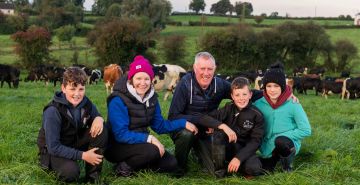 The Brennan family sitting in their field with cattle in the background.