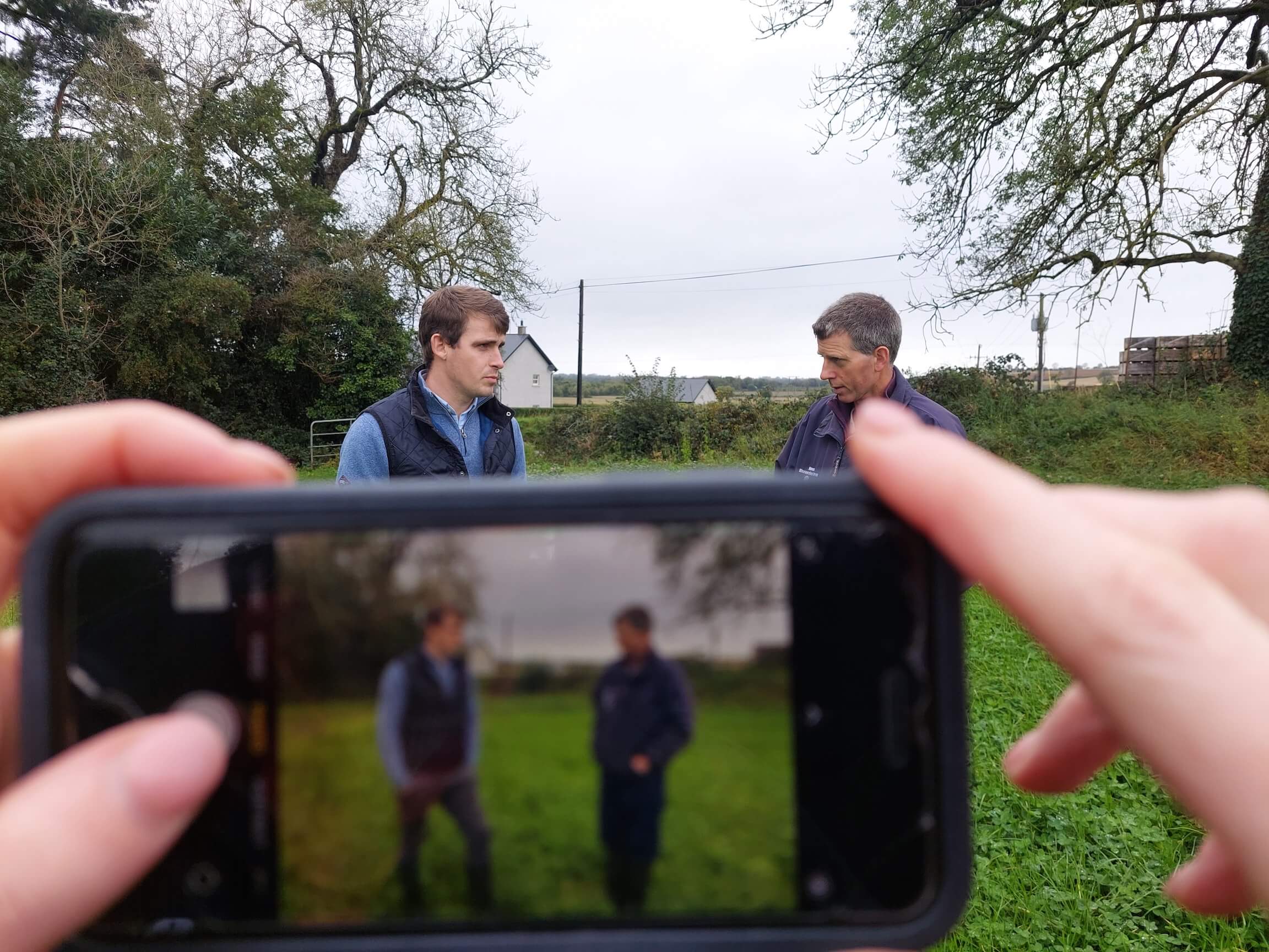 Someone using their phone to take a picture of a Lakeland Dairies employee and a milk supplier.