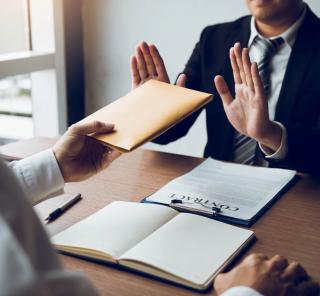 An anti-corruption image which represents an employee rejecting a brown envelope.