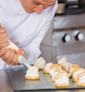 Chef piping Lakeland Dairies Whipping Cream onto a pastry base, with a plate of pastries filled with cream