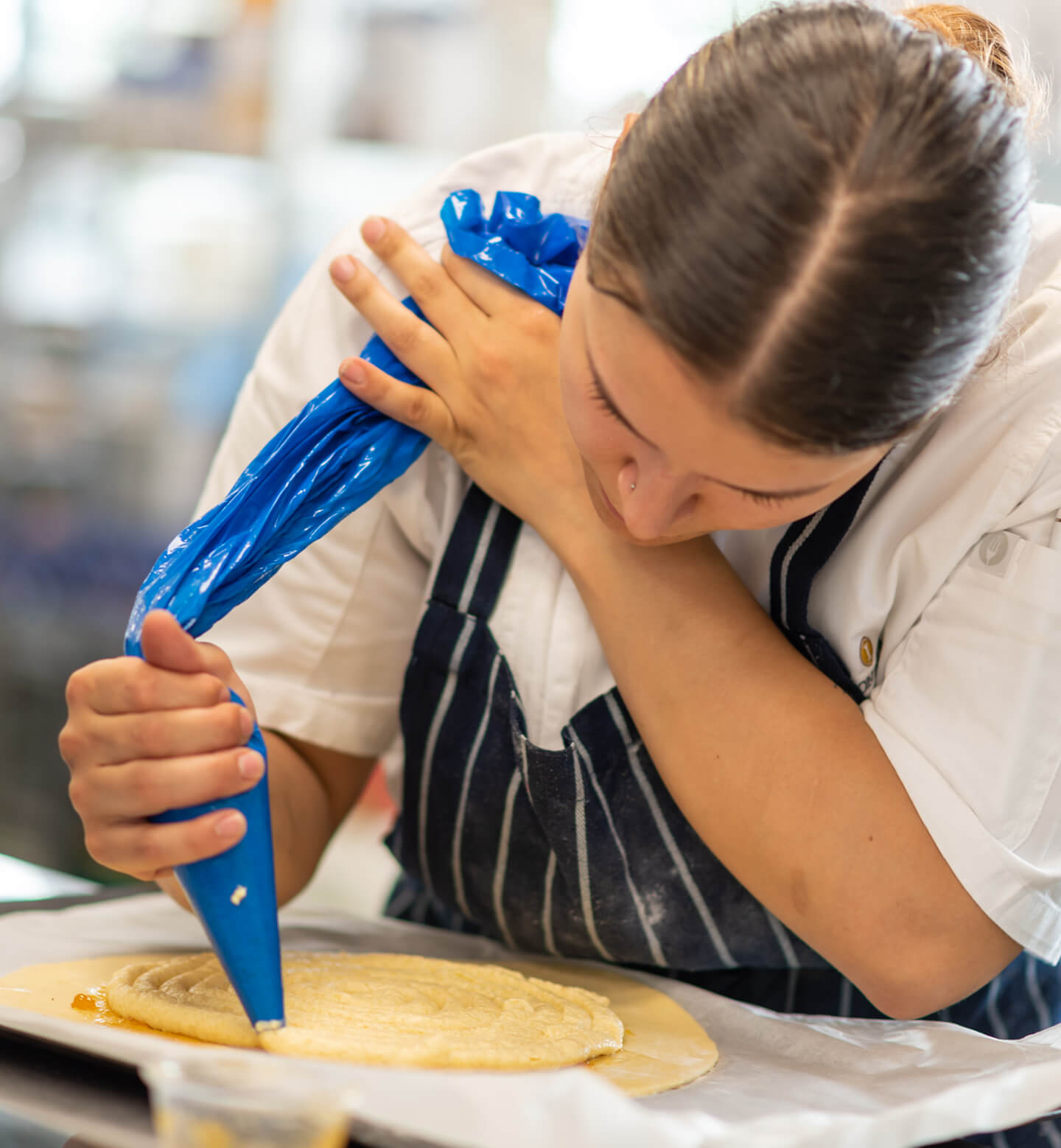 female chef piping cream onto a cake wearing chefs whites and a navy apron
