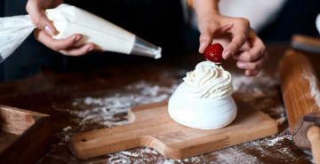 Chef piping cream from piping bag onto meringue dessert and placing raspberry on top