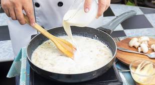 Frying pan with a creamy mushroom sauce, with close up of chef hands using wooden spatula to stir the sauce, whilst adding in more Millac Gold cream