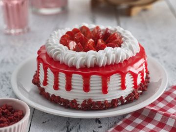 Cake topped with cream, strawberries and syrup on red table cloth