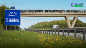 An image to represent the Lakeland Dairies Foundations For A Better Future strategy. A motorway with a Lakeland Dairies lorry travelling on it. Cattle crossing over the motorway on a bridge.