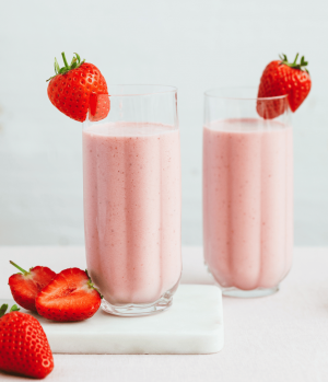 Two strawberry milkshakes in two glasses with fresh strawberries. Milkshakes made with Lakeland Dairies semi skimmed milk and skimmed milk powder