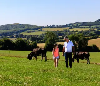 A Lakeland Dairies milk supplier walking with his daughters through fields with rolling hills in the background.