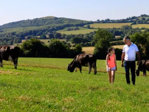 A Lakeland Dairies milk supplier walking with his daughters through fields with rolling hills in the background.